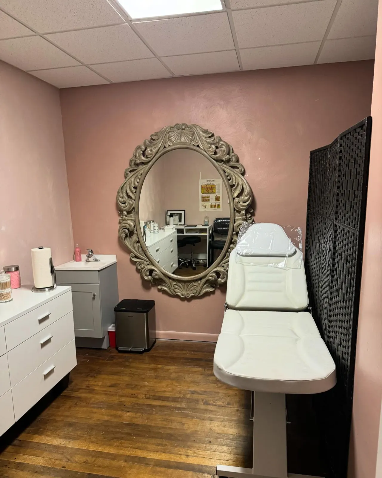 Treatment room with an ornate oval mirror and white treatment bed
