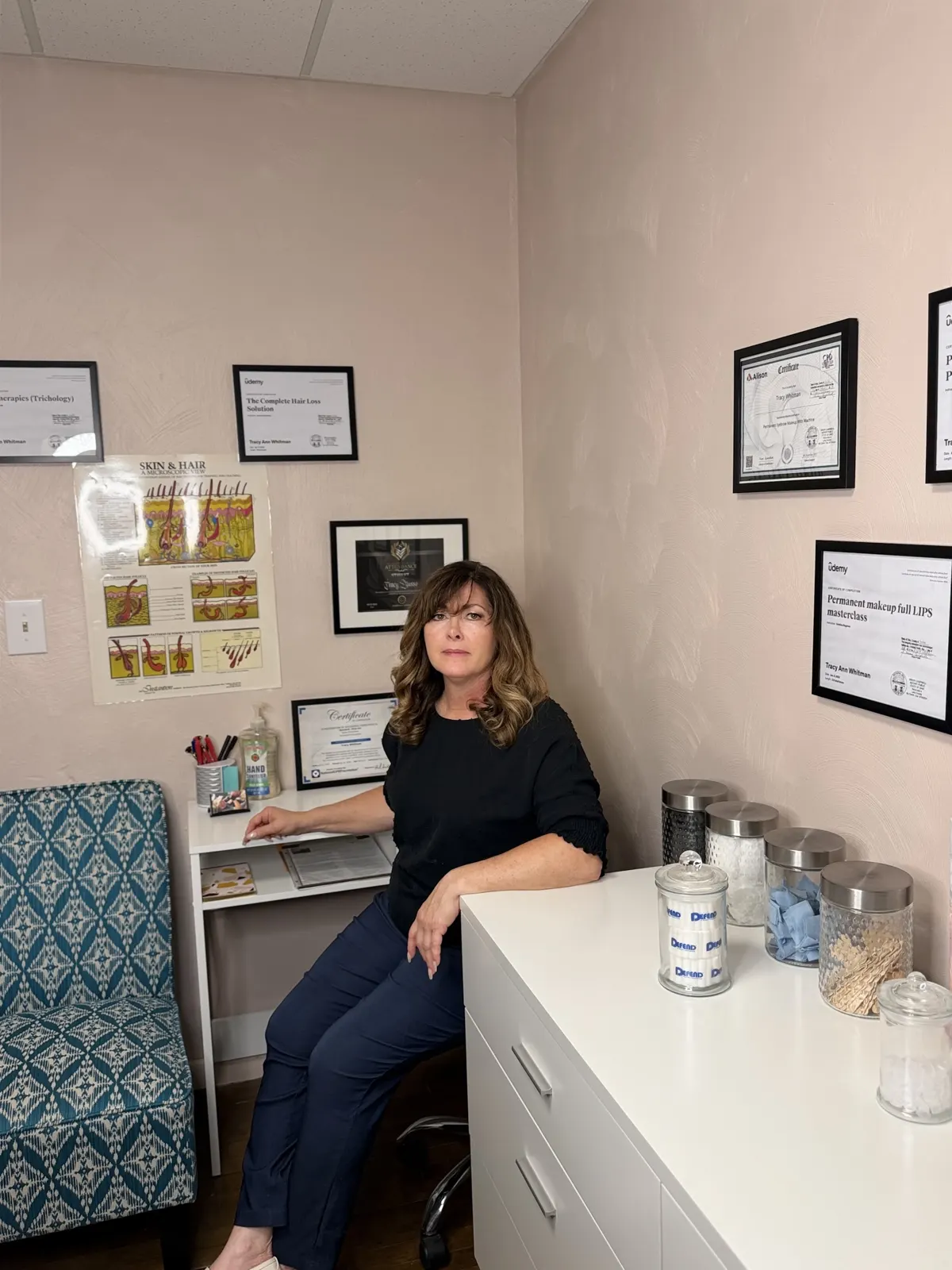 Tracy seated in her studio beside framed certificates